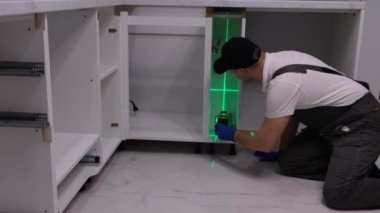 Kitchen fitter with an electronic level. High-quality and durable installation of furniture in a new apartment. Laser level when installing furniture