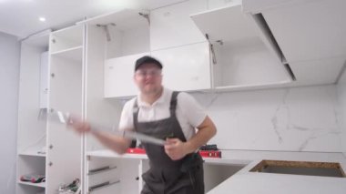 A crazy worker imitates playing the guitar while installing a kitchen. A cheerful craftsman at work