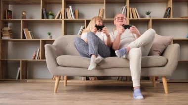 Mutlu emekli çift joystickle oyun oynuyor. Araba yarışı oyunundan büyülenen yaşlı bir çift evlerindeki kanepede televizyon ekranının önünde oturuyor. Emeklilerin mutlu hayatı