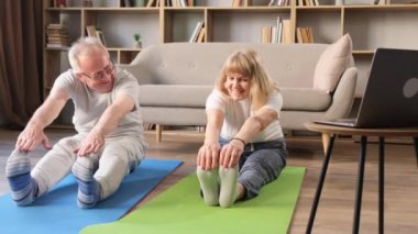 Yaşlı bir çift, güneşli bir sabahta evde birlikte jimnastik ve yoga yapıyor. Sağlıklı yaşam tarzı, fitness, eğlence. Emeklilik yaşında karı koca aktif ve sağlıklıdır..