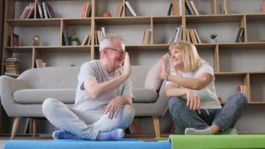 Evde yerde otururken sağlık egzersizi yapan mutlu çift. Emekliler sağlıklı bir yaşam sürüyorlar.