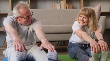 Büyükbabalar jimnastik ve esneme egzersizleri yapar. Yaşlılıkta sportif bir aile çifti. Mutlu emekliler.