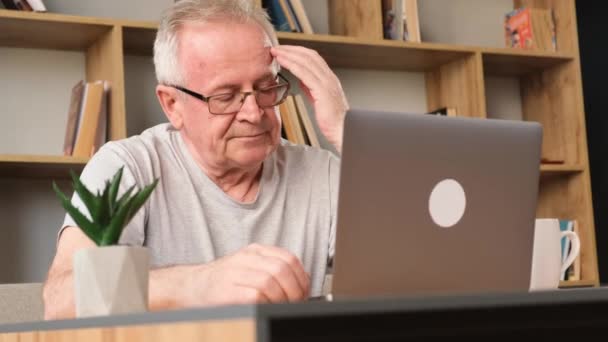 累了的祖父坐在客厅的沙发上 在笔记本电脑上工作 头痛的退休人员在计算机上工作 — 图库视频影像