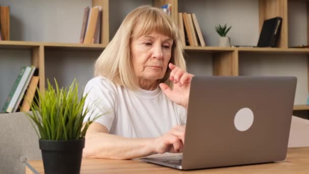 累坏了的祖母坐在客厅的沙发上 在笔记本电脑上工作 一个退休的女人在电脑前工作 — 图库视频影像