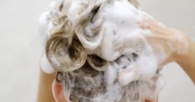 Genç bir kız saçını şampuanla yıkar. Bir kadın duş alıyor. Saçlarını yıkamak için ellerini kullanıyor. Saç bakımı