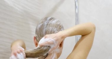 Sıcak bir duş deryasının altında genç bir kadın elleriyle saçlarına masaj yapıyor. Kafasını şampuanla yıkamak. Güzel, uzun saçlara dikkat et..