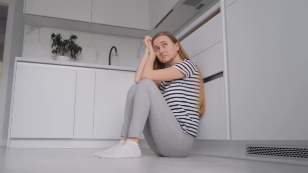 台所の床にはヨーロッパ人の疲れた女が腰を下ろしている うつ病と絶望の女性 — ストック動画