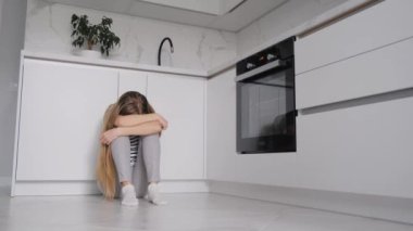Depresyondan muzdarip bir kadın, mutfak odasında oturuyor, başını dizlerinin arasına sakladı. 4k video