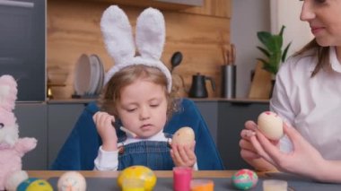 Anne ve kızı Paskalya için yumurta boyuyor. Mutlu bir aile tatil için hazırlanıyor. Tavşan kulağı takan tatlı küçük bir kız. 4k video