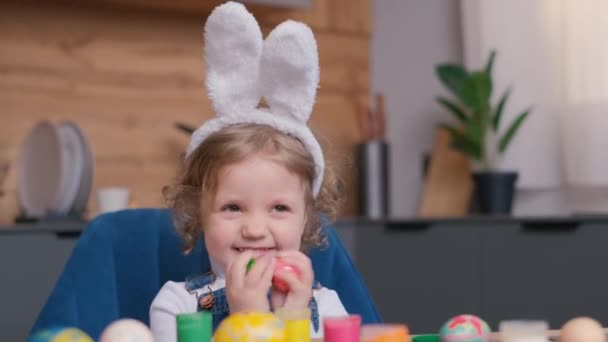 一个长着小兔子耳朵的女孩在厨房桌上玩复活节彩蛋 复活节假期的概念 — 图库视频影像