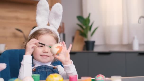 Dziewczyna Króliczymi Uszami Maluje Wielkanocne Jajka Przy Stole Kuchennym Koncepcja — Wideo stockowe
