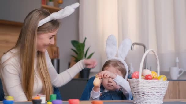 一位年轻的母亲和她的女儿为复活节彩绘彩蛋 他们穿着兔子耳朵的衣服 复活节假期的概念 4K视频 — 图库视频影像