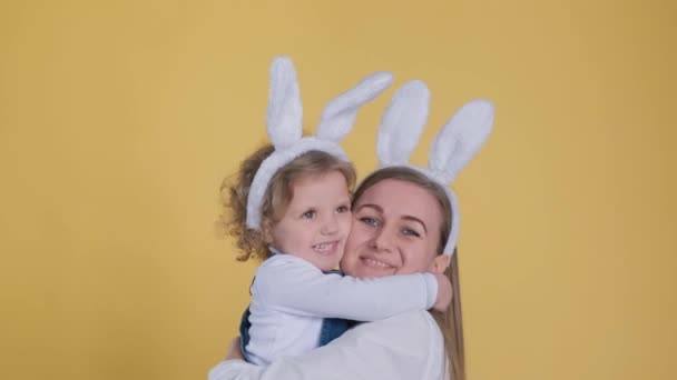 迷人的年轻女子与可爱的小女孩在兔子的耳朵亲吻 拥抱孤立的黄色背景 — 图库视频影像