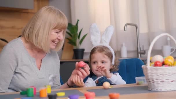 祖母と孫娘はイースターのために卵をペイントし 彼らはウサギの耳に身を包んだ イースター休暇のコンセプト 4Kビデオ — ストック動画