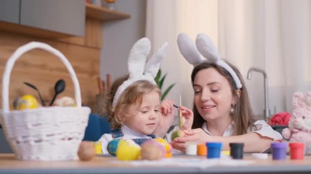 母親と娘は台所でイースターエッグを描きます 幸せな家族はイースターの準備をしています イースターのウサギの耳のかわいい女の子 ハッピーイースター — ストック動画