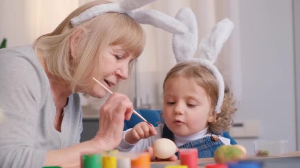 奶奶和她的家人为复活节彩绘彩蛋 他们穿着兔子耳朵的衣服 复活节假期的概念 4K视频 — 图库视频影像