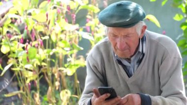 Yaşlı bir büyükbaba akıllı telefon kullanmayı öğreniyor. Gri saçlı büyükbaba telefonda video izliyor.