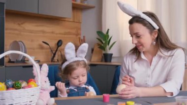 Anne ve kızı yumurta çekiyor. Küçük şirin bir kız bebek tavşan kulağı takıyor..