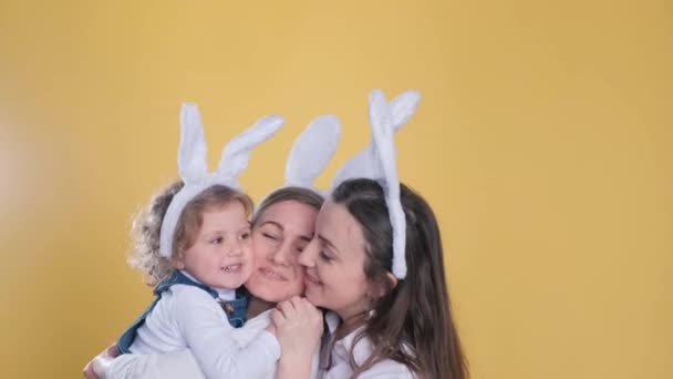 年轻的母亲和两个女儿 有一对黄色背景的小兔子耳朵 复活节庆祝活动 — 图库视频影像