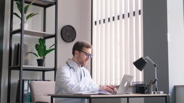 严肃的治疗师在网上写报告或咨询病人 填写医疗卡 戴着眼镜在笔记本电脑上工作的年轻医生 — 图库视频影像