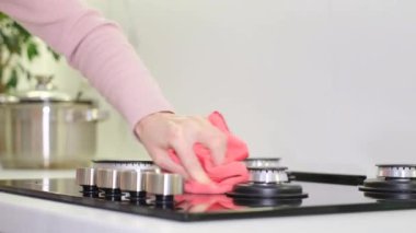 Eldiven giymiş bir kadın mutfakta metal bir sobayı bez parçasıyla siler. Modern mutfak aletleri