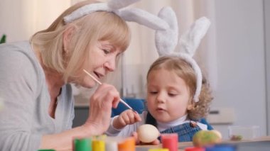 Büyükanne ve ailesi Paskalya için yumurta boyuyor, tavşan kulağı takıyorlar. Paskalya tatili konsepti. 4k video