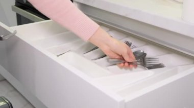 Bir kadının eli mutfak gereçlerini çekmeceye koyar. Çatallar, kaşıklar ve bıçaklar için mutfak kutusu..