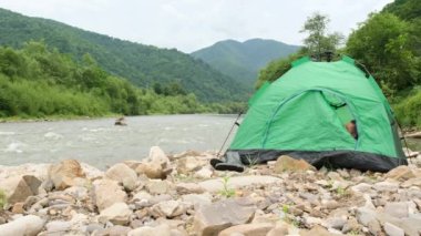 Genç bir Avrupalı adam hızlı bir nehrin yanındaki dağların arasında yeşil bir çadırda yatıyor. Issız bir yerde huzur içinde yat..