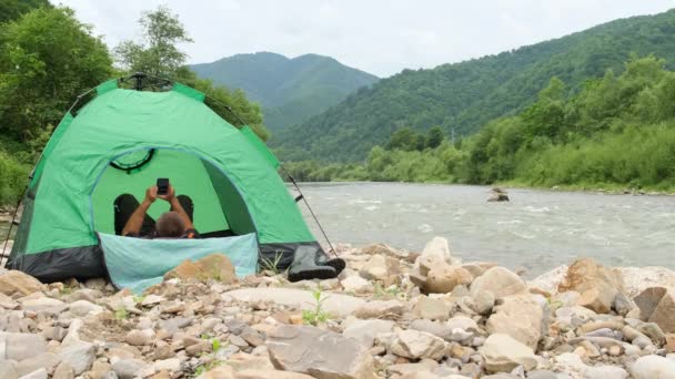 Seorang Turis Bersandar Tenda Hijau Tepi Sungai Pegunungan Melihat Telepon — Stok Video