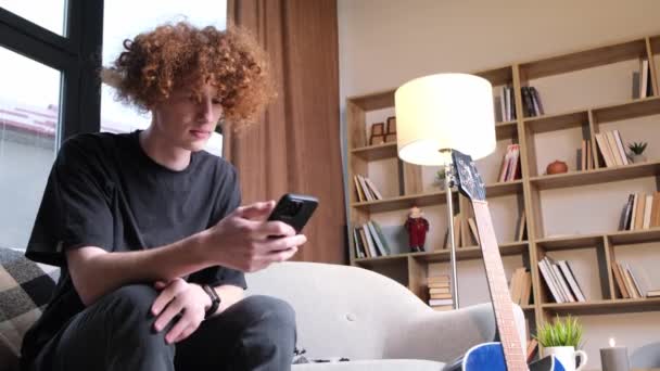 Kıvırcık Saçlı Bir Adam Telefonda Internette Modern Bir Oturma Odasında — Stok video