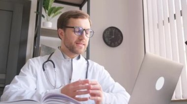 Beyaz önlüklü, güler yüzlü erkek doktor hastalara uzaktan tanı ve tedavi sunuyor.. 