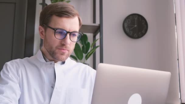 Bilgisayarda Çalışan Gözlüklü Beyaz Üniformalı Ciddi Genç Doktor — Stok video