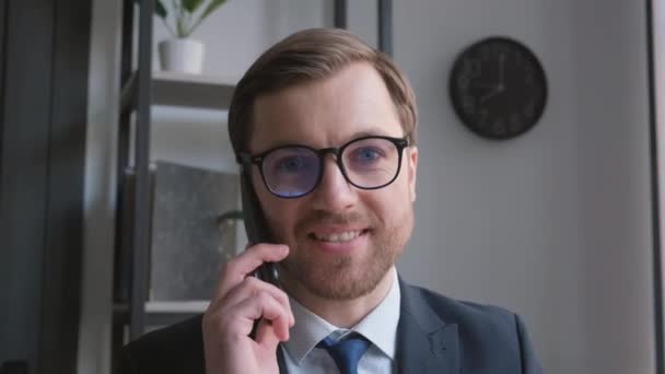 一位自信的年轻商人坐在办公室里 一边用手机交谈 一边与他亲密接触 具有欧洲风貌的银行雇员的工作 — 图库视频影像