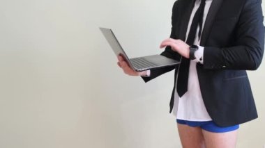 Pantolonu olmayan iş ceketli bir adam dizüstü bilgisayar tutuyor ve internette biriyle konuşuyor. Beyaz bir duvarın karşısında iç çamaşırlı bir iş adamı..