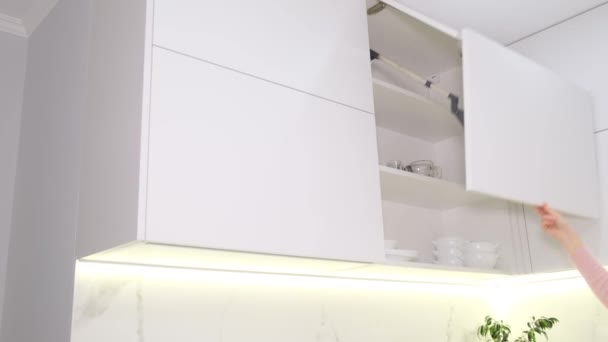 一个女人的手打开一个大厨房柜 放了一个盘子在那里 白色的新现代厨房 — 图库视频影像