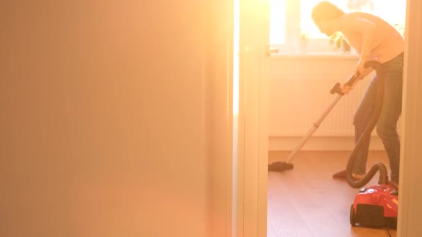 Seorang Wanita Memvakum Lantai Sebuah Ruangan Dengan Latar Belakang Sinar — Stok Video