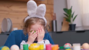 Tavşan kulaklı mutlu çocuk Paskalya için evi süslüyor, boyalı yumurtalarla oynuyor, gözlerini kapıyor. Yüksek kalite 4k video