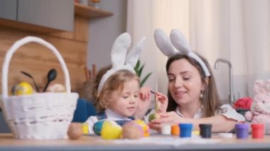 Anne ve kızı mutfak odasına paskalya yumurtası çiziyor. Mutlu bir aile Paskalya için hazırlanıyor. Paskalya için tavşan kulaklı şirin bir kız. Mutlu Paskalyalar