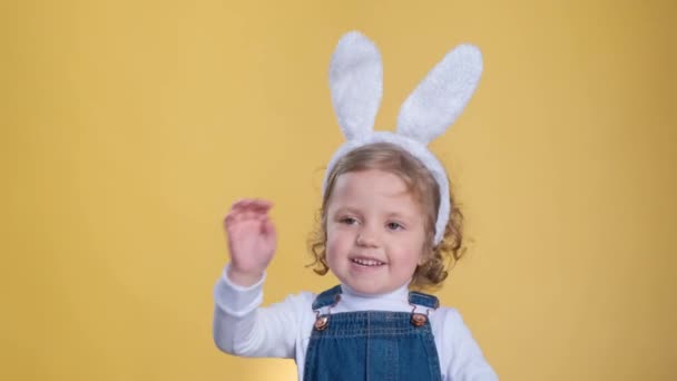 黄色の背景にイースターバニーの耳を持つかわいい女の子がペンを振っています イースター 春のコンセプト — ストック動画