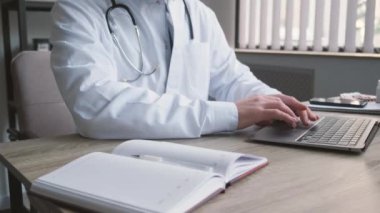 Genç yakışıklı bir doktor ofisinde bir dizüstü bilgisayar üzerinde çalışıyor. Avrupa 'da modern bir sağlık kliniği.