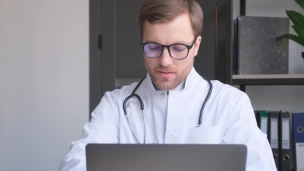若いハンサムな医者が彼のオフィスのノートパソコンで働いている ヨーロッパの近代的な医療機関 — ストック動画
