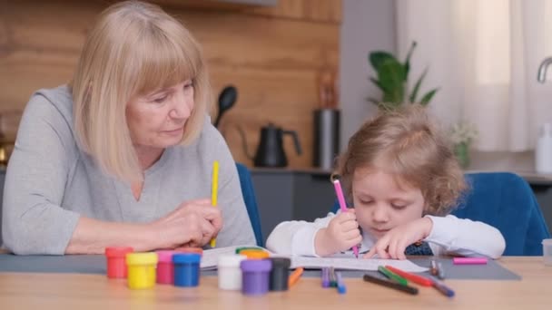 祖母は孫に台所のテーブルに座って絵を描くように教える 鉛筆で子供の絵を描く 4Kビデオ — ストック動画