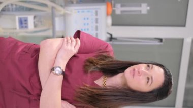 Özel elbiseli güzel bir kadın doktorun kliniğinin ofisinde dikey videosu. Doktor kameraya özgüvenle bakar ve gülümser. 4k video