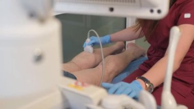 Profesyonel bir doktor klinikteki diz eklemini ultrasonla muayene eder. Doktor diz bölgesine ses dalgaları göndermek için dönüştürücü kullanıyor.