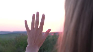 Genç bir kadın, bir tarlada güzel bir günbatımında elini tutuyor. 4k video