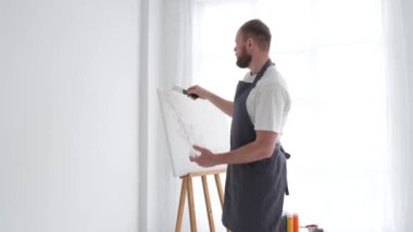 Profesyonel bir sanatçı beyaz bir tuvale metal bir fırça ve sehpa kullanarak resim çizer. Bir sanatçının alçıdan bir resim yapma süreci.