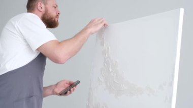 Yetenekli bir erkek sanatçı, fırça kullanarak, beyaz bir tuvalde yağlı boya tablosunun modern bir başyapıtını yaratıyor. Tuval büyük bir stüdyoda bir sehpanın üzerinde..