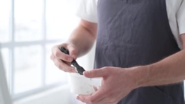 Yetenekli bir erkek sanatçı, fırça kullanarak, beyaz bir tuvalde yağlı boya tablosunun modern bir başyapıtını yaratıyor. Tuval büyük bir stüdyoda bir sehpanın üzerinde..