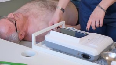 Bir kadın kardiyolog yaşlı bir erkek hastanın vücuduna elektrokardiyogram ya da EKG için plastik vakum sensörleri yerleştiriyor. Kalp hastalıkları