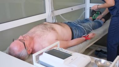 Bir kadın kardiyolog yaşlı bir erkek hastanın vücuduna elektrokardiyogram ya da EKG için plastik vakum sensörleri yerleştiriyor. Kalp hastalıkları